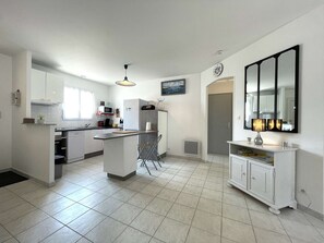 A modern kitchen with white cabinetry, a central island, and a dining area with a white table and chairs. - Vacation home 3 bedrooms in Bretignolles-sur-Mer (Bretignolles-sur-Mer)