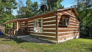 Une cabane en rondins avec un porche, une antenne parabolique et une petite terrasse.