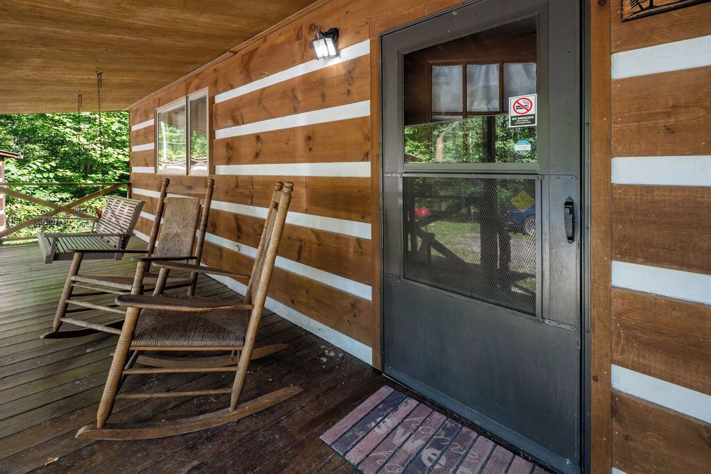 Uma cabana de madeira com varanda, cadeiras de balanço e uma porta com mosquiteiro.