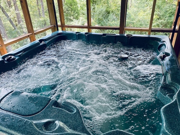 Un bain à remous avec vue sur une forêt, grâce à de grandes fenêtres.