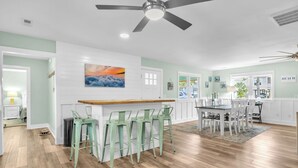 A spacious kitchen with a dining area, featuring a wooden floor, white cabinetry, and a ceiling fan. - Poolside Paradise: Modern Coastal Oasis with Private Backyard Pool (Oak Island)