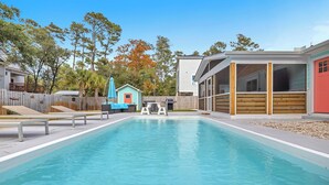 A swimming pool with a wooden deck, a small shed, and a covered area with windows. - Poolside Paradise: Modern Coastal Oasis with Private Backyard Pool (Oak Island)