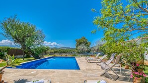 Une piscine entourée de verdure, avec des chaises longues et des serviettes à disposition, sous un ciel dégagé.