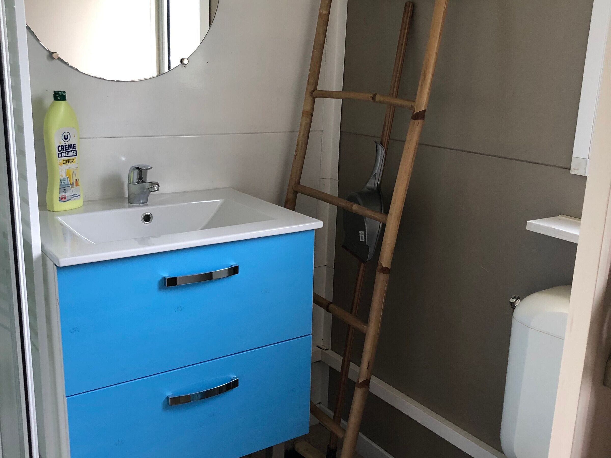 Une salle de bain avec un lavabo blanc, un meuble bleu et une échelle appuyée contre le mur.