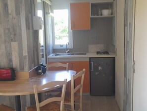 A compact kitchen with a sink, a small refrigerator, and wooden chairs around a table.