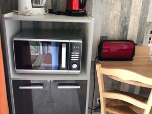 Une cuisine équipée d’un micro-ondes, d’un grille-pain et d’une machine à café, le tout placé sur une étagère.