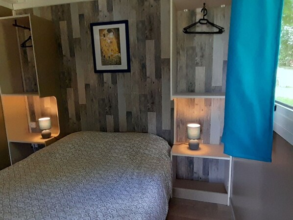 Une chambre à coucher avec une couvre-lit à motifs, deux tables de chevet avec des lampes, une œuvre d’art encadrée au mur et un rideau bleu.
