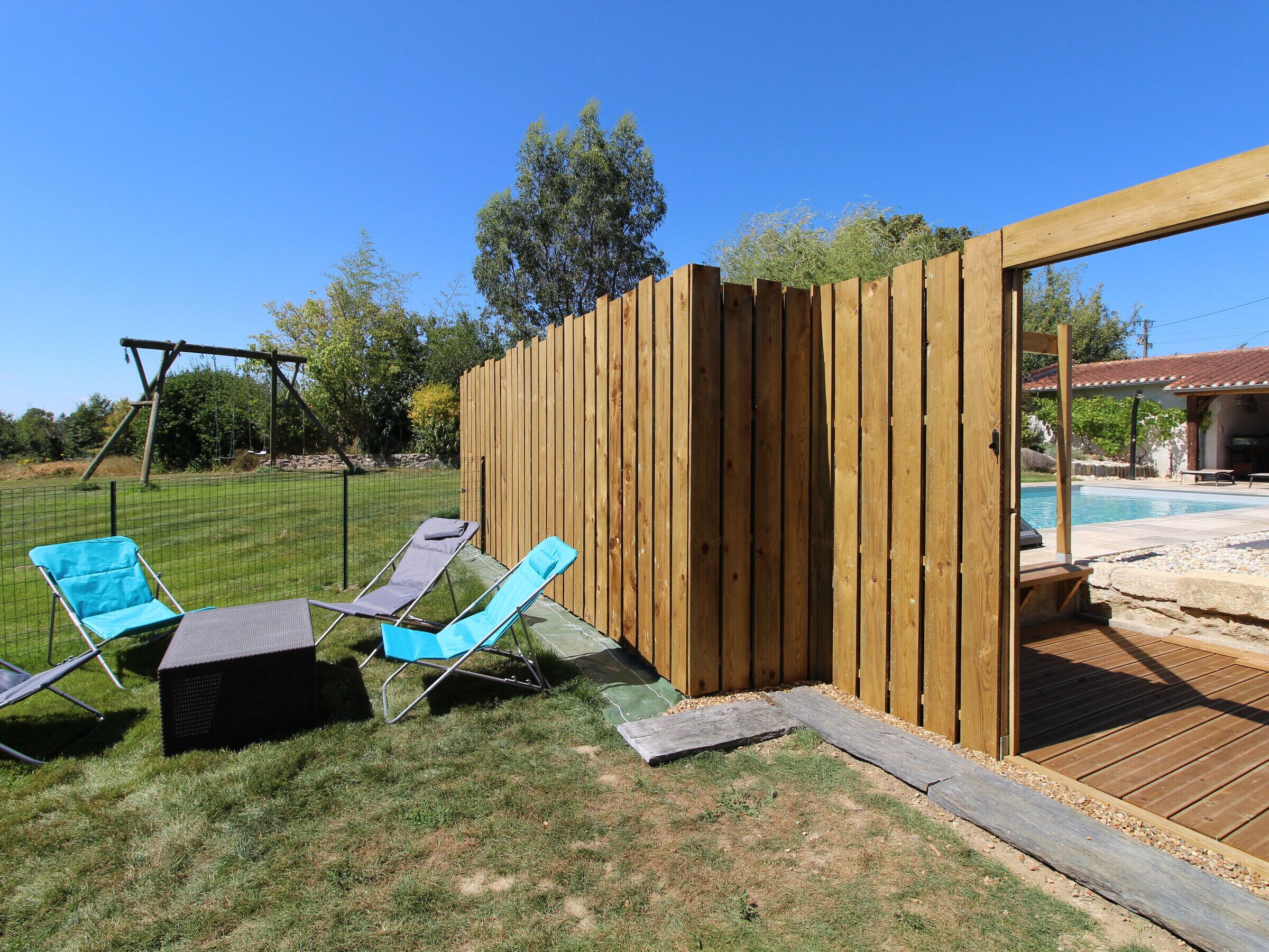 A backyard with a wooden fence, a swing set, and two blue lawn chairs.