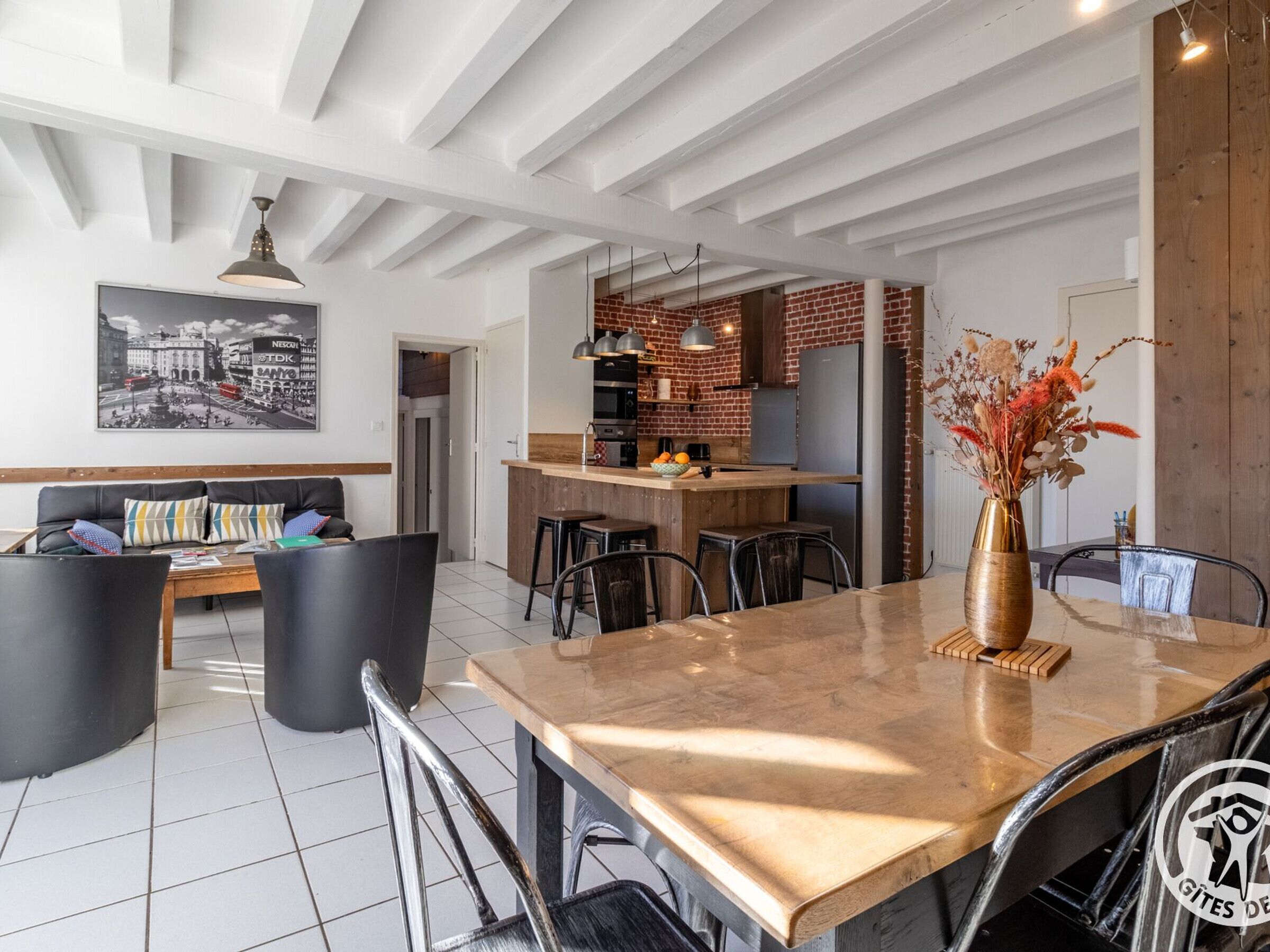 A modern kitchen with a brick backsplash, a dining area with a marble table, and a living room with a sofa and chairs.