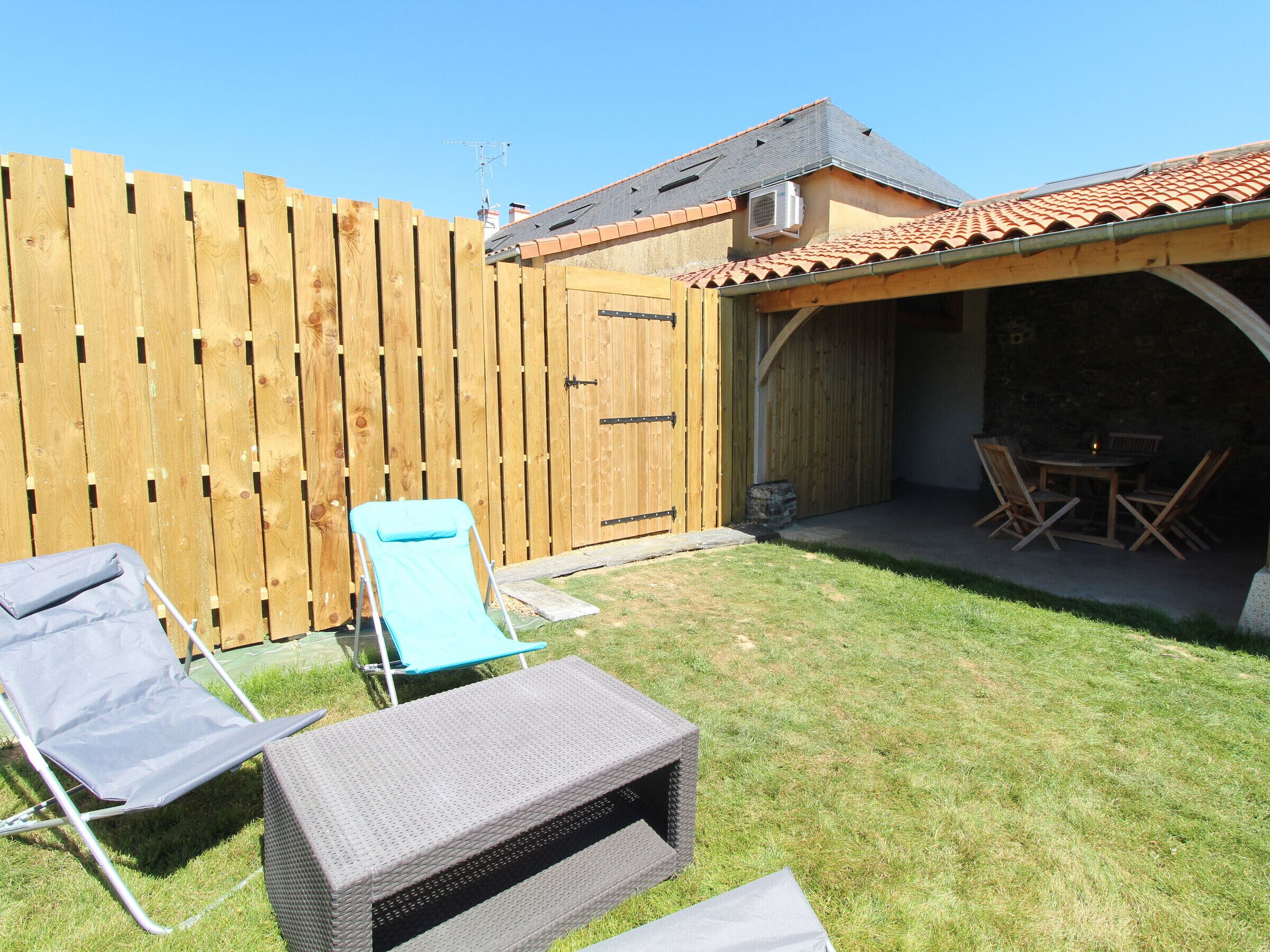 A backyard with a wooden fence, a covered patio area, and outdoor furniture including a table and chairs.