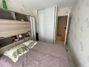 Et soveværelse med en seng, et garderobeskab, en hylde med en lampe og et lille bord med en dukke.