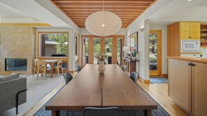 Een moderne keuken met houten kastjes, een centraal eiland en een eethoek met een lange tafel en stoelen.