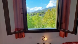 A room with two beds, a window with curtains, a table with a lamp, and a view of greenery and hills. - Villa (Reggello)