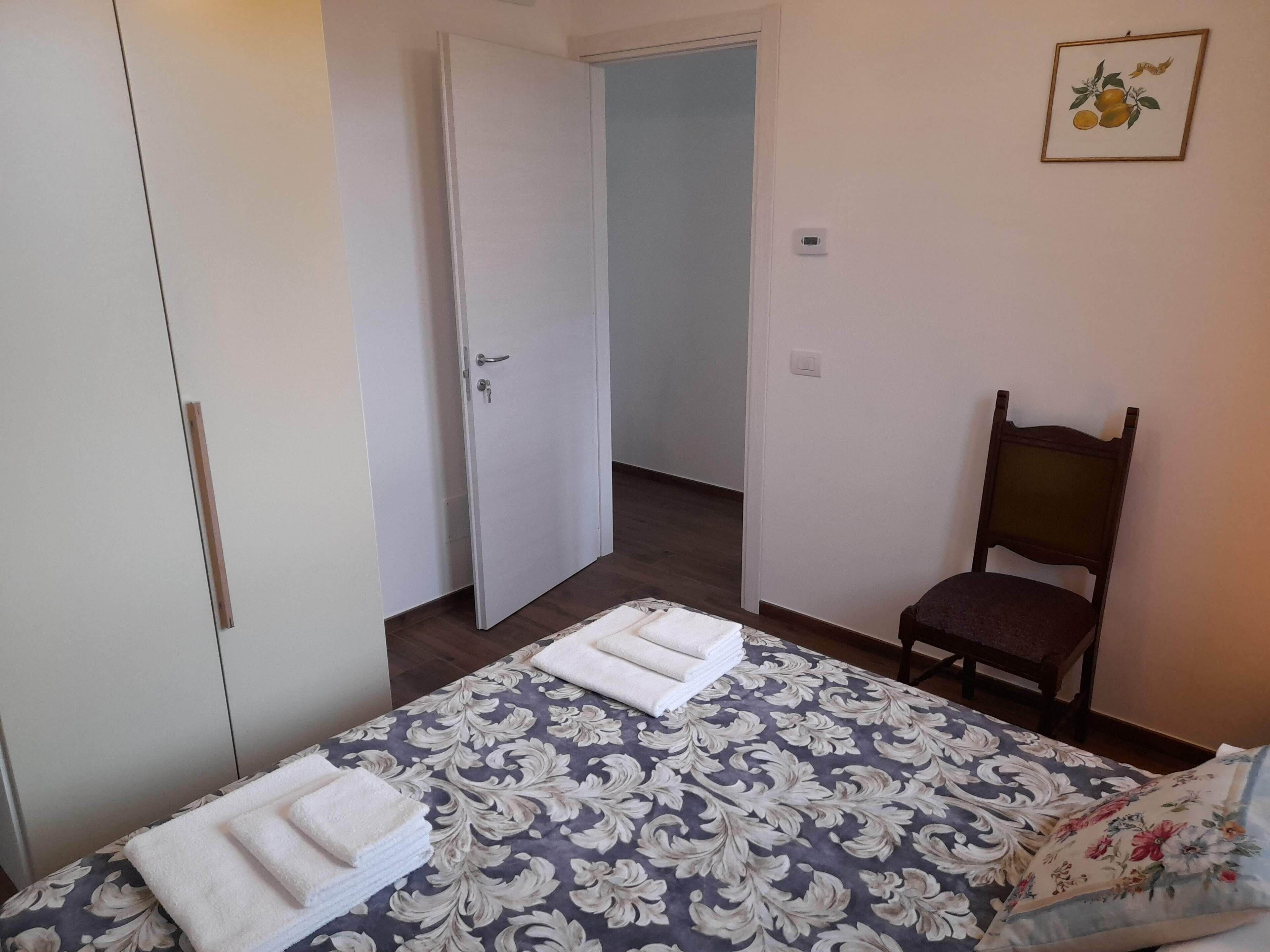 Un dormitorio con cama, una silla, armario y puerta.