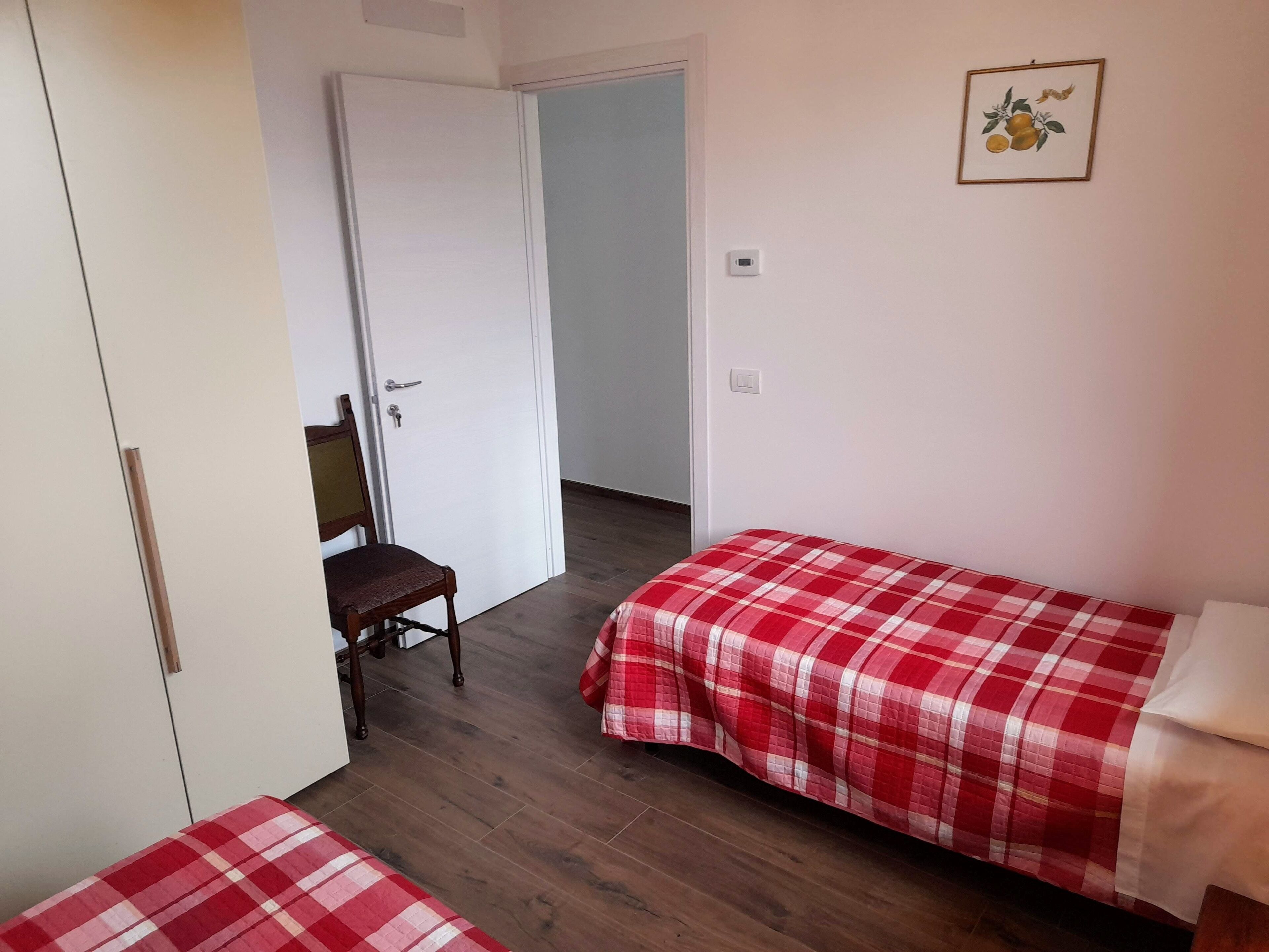 A room with two beds, a wooden chair, a white wardrobe, and a door leading to another room.