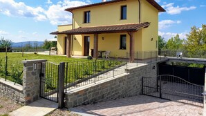 A two-story yellow building with a tiled roof, a stone entrance gate, and a paved pathway leading to the entrance. - Villa (Reggello)