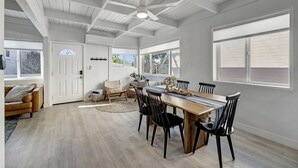 A spacious dining area with a wooden table and black chairs, a ceiling fan, and large windows with blinds. - Bright Beach access retreat w/ AC (Laguna Beach)