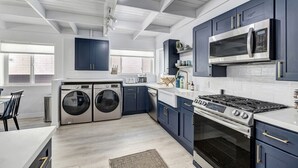 A modern kitchen with built-in appliances, a dining area with a table and chairs, and a laundry area with washing machines. - Bright Beach access retreat w/ AC (Laguna Beach)