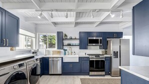 A modern kitchen with dark blue cabinets, stainless steel appliances, and a large window providing natural light. - Bright Beach access retreat w/ AC (Laguna Beach)