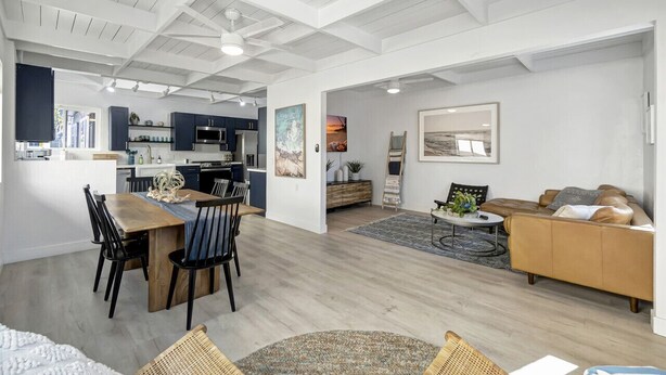 A spacious living area with a wooden dining table, a sofa, and a kitchen in the background. - Bright Beach access retreat w/ AC (Laguna Beach)