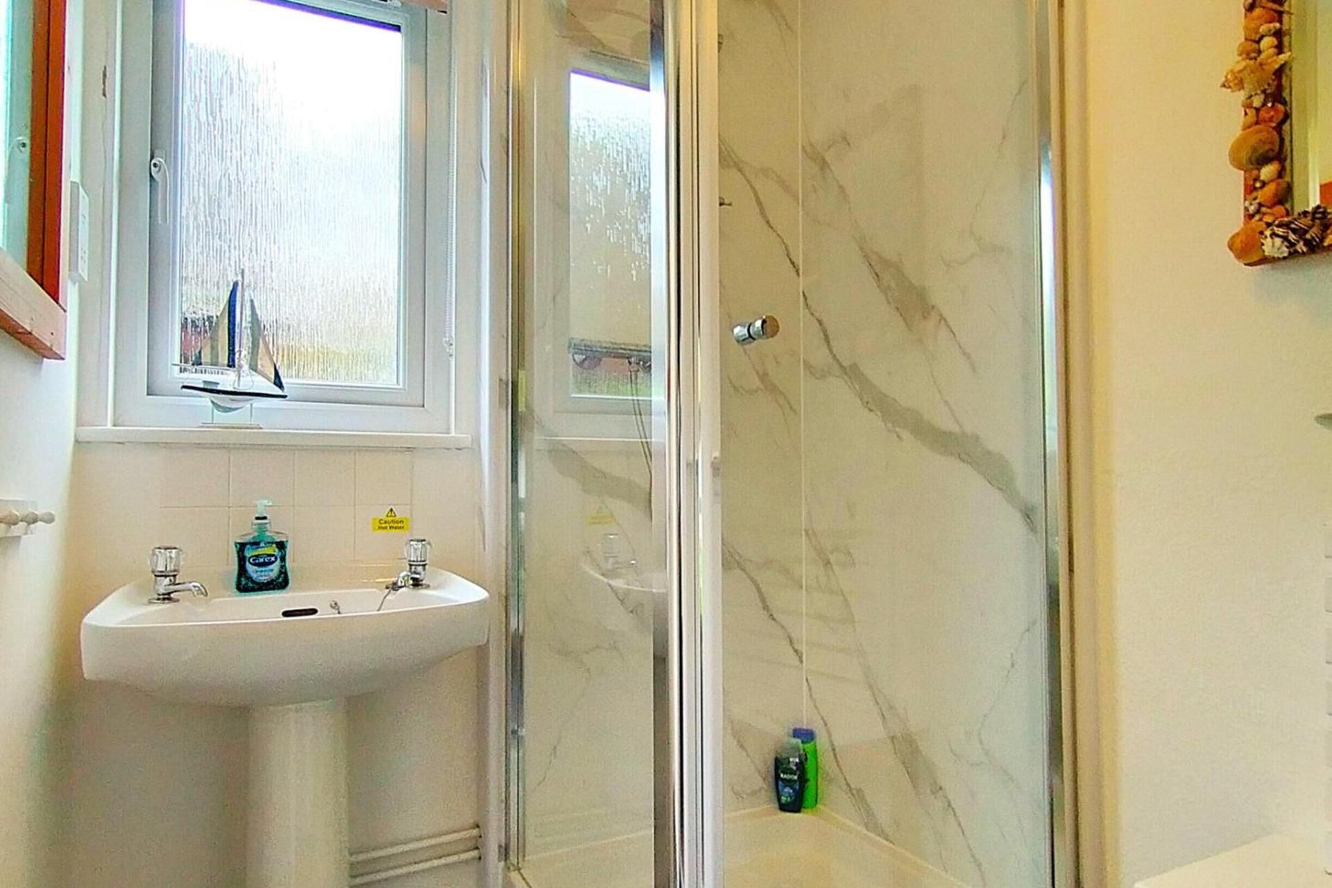 Une salle de bain avec un lavabo blanc, une cabine de douche en verre et un mur en marbre.