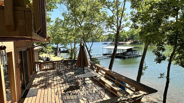 A wooden deck with outdoor furniture, overlooking a lake with docks and boats. - Updated Ozarks Lakefront Home-Lilly pad, kayaks, Private dock & boat ramp. (Sunrise Beach)