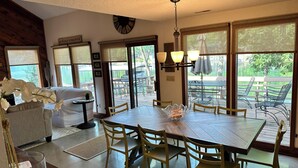 Comedor con mesa y sillas de madera, una araña y ventanas amplias con vistas al exterior.