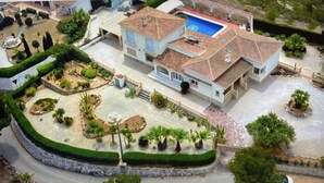 Une grande maison avec une piscine, entourée d’un jardin bien entretenu et d’une allée pavée.