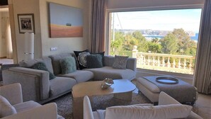 Un salon moderne avec un canapé d’angle, une table basse et une vue sur la mer grâce à de grandes fenêtres.