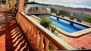 Une piscine avec un pont, entourée d’une terrasse couverte avec des chaises et une table.
