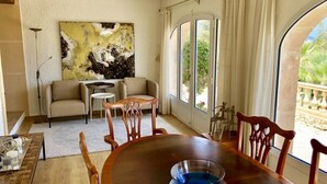 Un coin repas avec une table en bois, des chaises et un bol bleu. On y trouve également un canapé et un tableau accroché au mur.