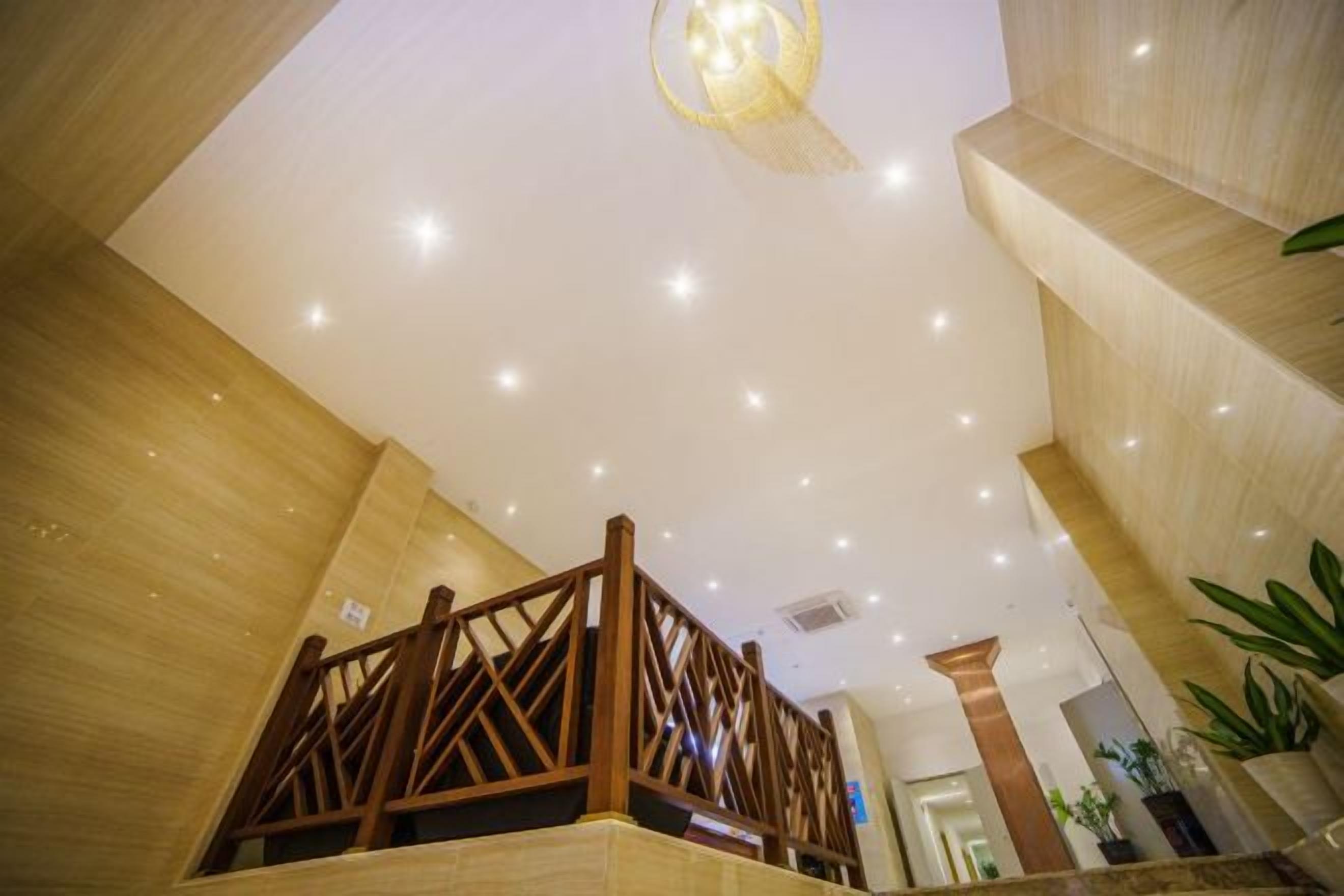 A hotel lobby with a wooden staircase, a chandelier, and a modern ceiling design.