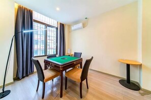 A room with a pool table, four chairs, a lamp, a small table, and a window with curtains. - Junchao Light Luxury Hotel (Zhuhai)