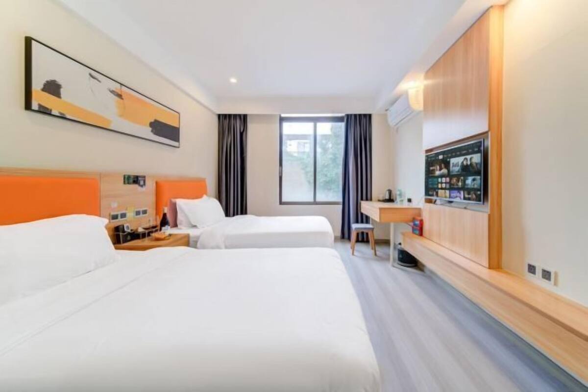 Habitación de hotel con dos camas, un escritorio, un televisor y una ventana con cortinas.