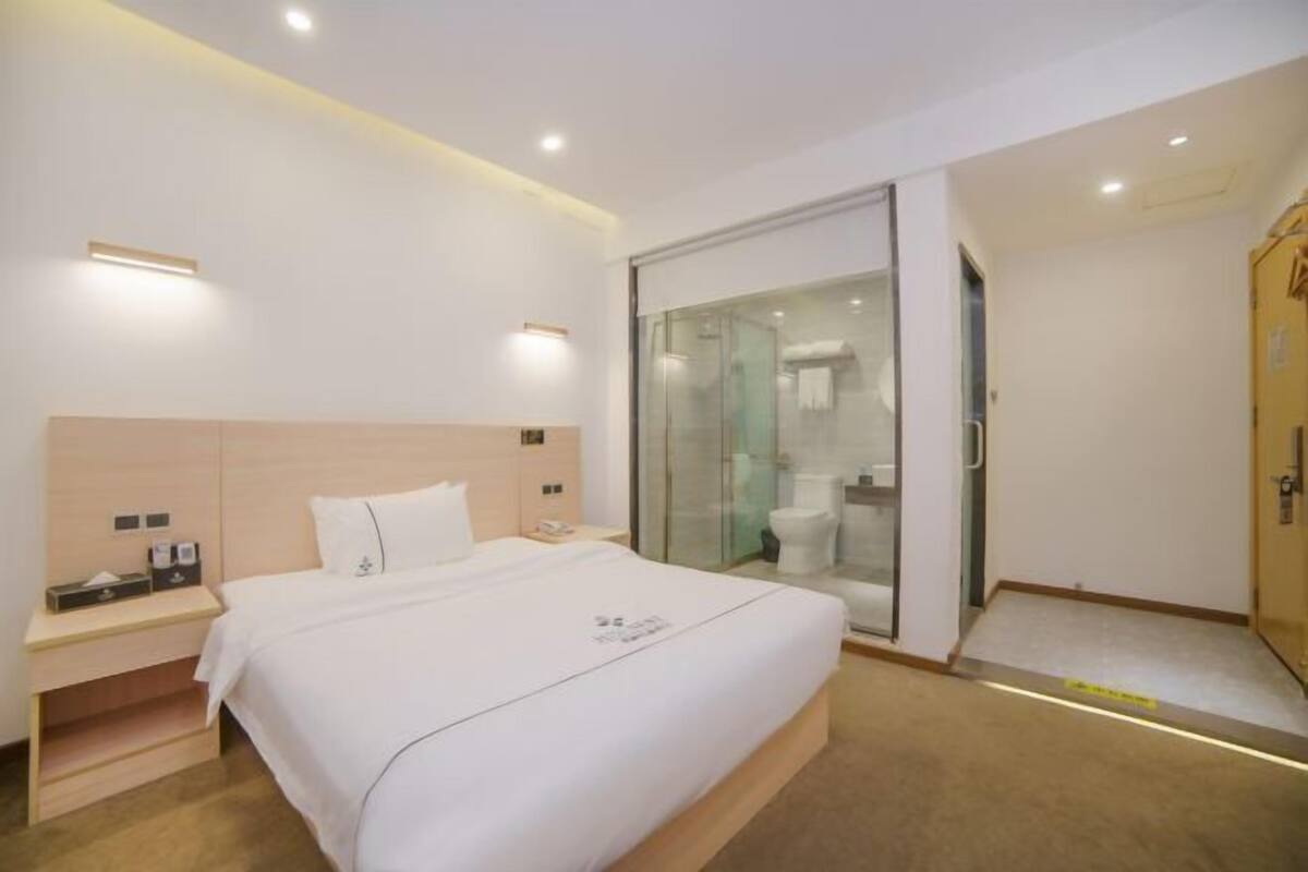 Habitación de hotel con cama, mesita de noche y puerta corredera de cristal que da a un baño.