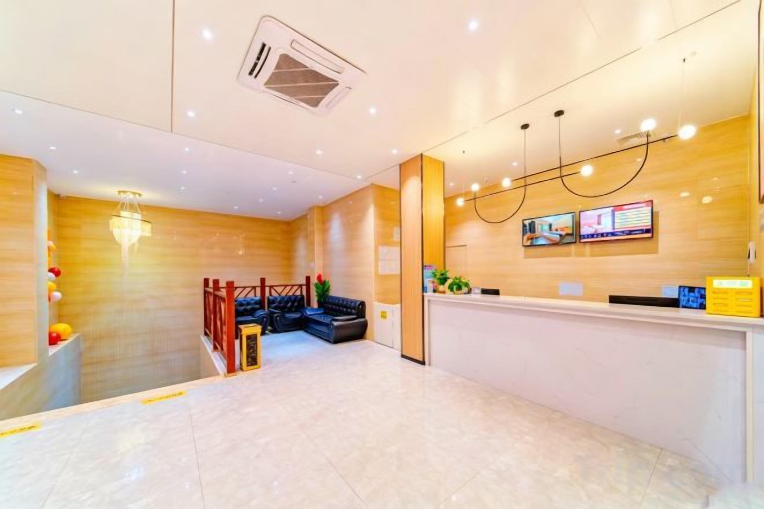 A hotel reception area with a wooden reception desk, a digital display, and a staircase leading to an upper level.