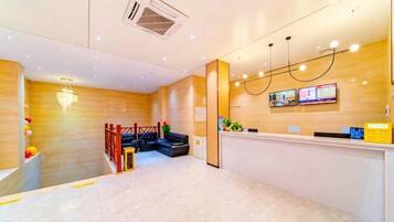 A hotel reception area with a wooden reception desk, a digital display, and a staircase leading to an upper level.