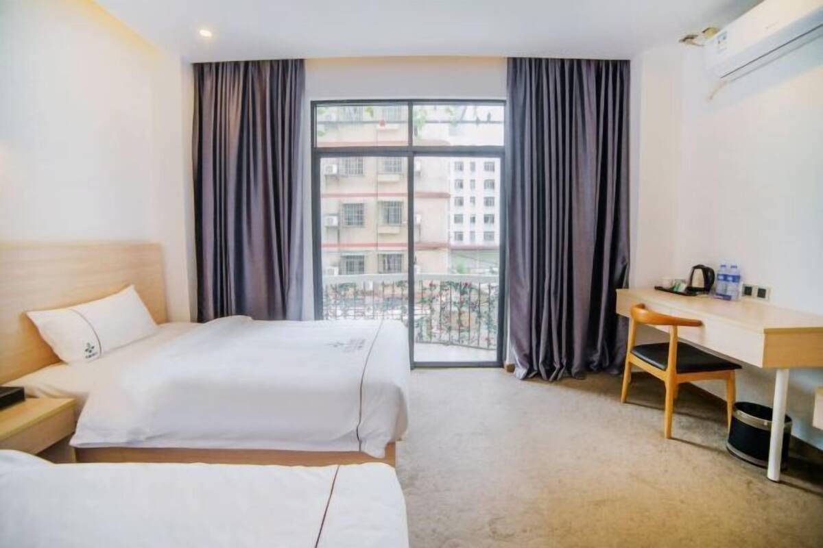 Habitación de hotel con dos camas, un escritorio, una silla y un ventanal con cortinas.