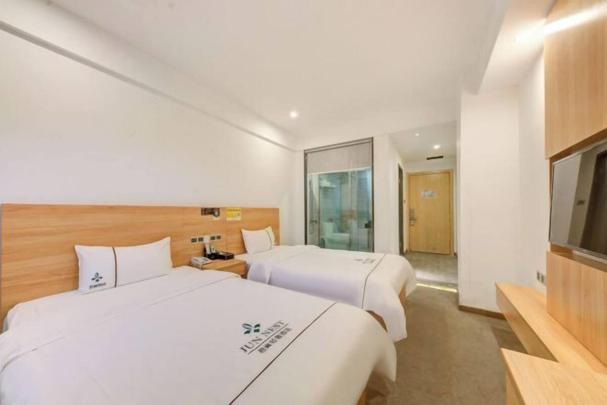 Una habitación de hotel con dos camas, televisión y cabecera de madera.