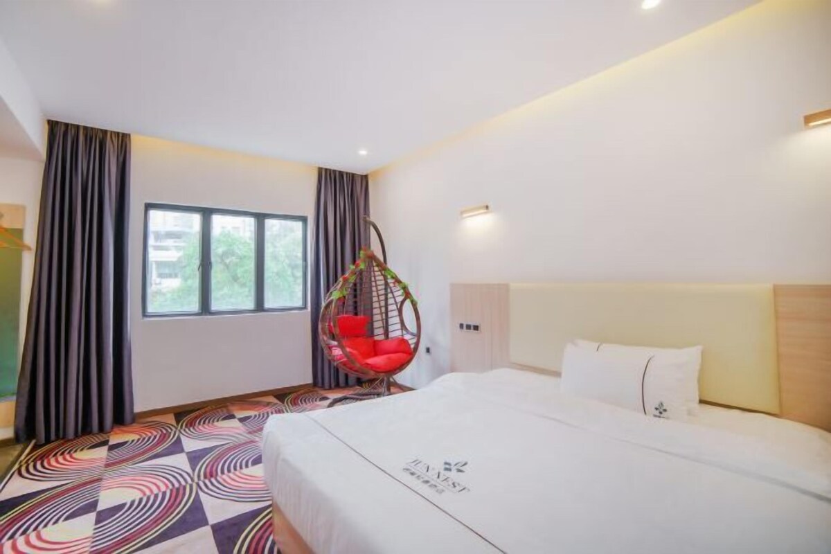 A hotel room with a large bed, a hanging chair, and a window with curtains.