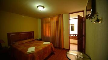 Quarto de hotel com uma cama, uma mesinha, uma porta que dá para uma varanda e uma luminária no teto.