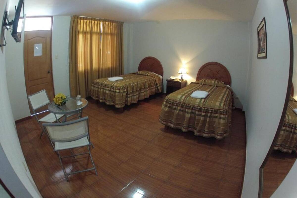 A hotel room with two beds, a small table with chairs, a desk, and a window with curtains.