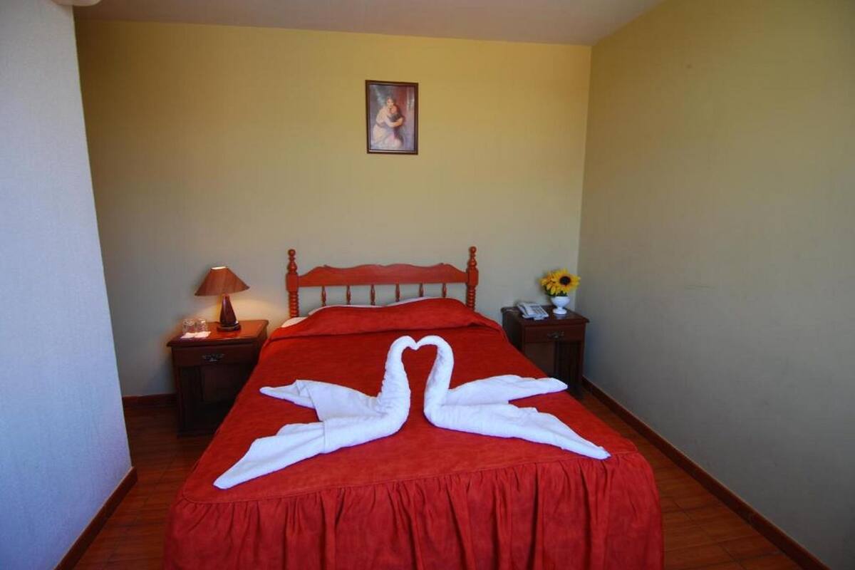 A hotel room with a bed, a nightstand with a lamp, a vase with flowers, and a framed picture on the wall.