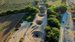 An aerial view of a field with circular pits and a dirt road. - Hotel Alegria Nasca (Nazca)