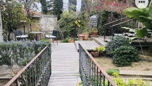 Une terrasse en bois qui mène à un espace patio aménagé avec des meubles d’extérieur et des plantes en pot.