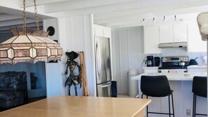 Une cuisine moderne avec des meubles blancs, un réfrigérateur en acier inoxydable, une cuisinière noire et une table à manger en bois.