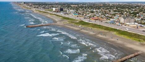 An aerial view of a coastal city with a beach, buildings, and a road.
