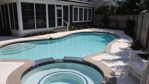 Una piscina con jacuzzi, rodeada por una terraza y una zona de estar cubierta.