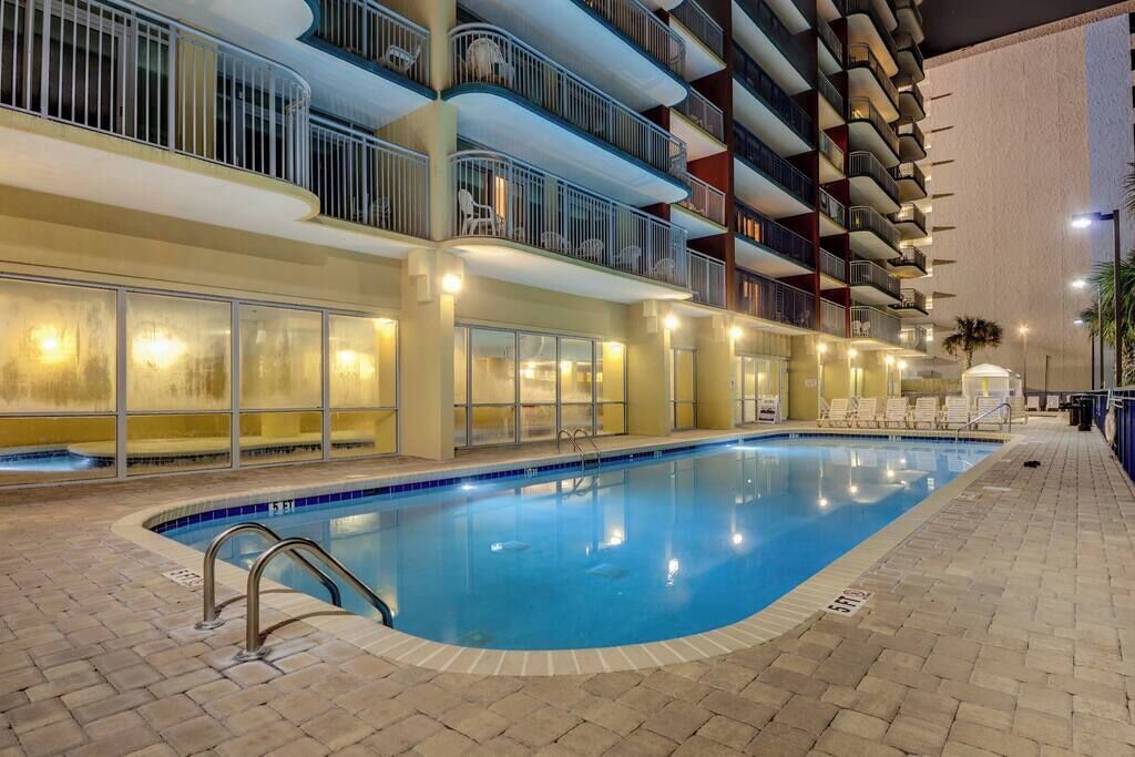 An indoor swimming pool with a tiled deck, surrounded by a multi-story building with balconies.