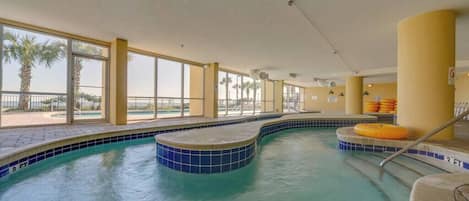 Una piscina interior con agua azul cristalina, borde de azulejos y vistas a palmeras al exterior.